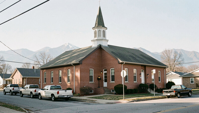 A mid-century brick church building on a quiet small-town American street with distant mountains behind it.